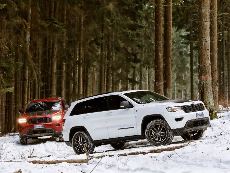 2017 red and white jeep grand cherokee trailhawk driving throught the woods on snow