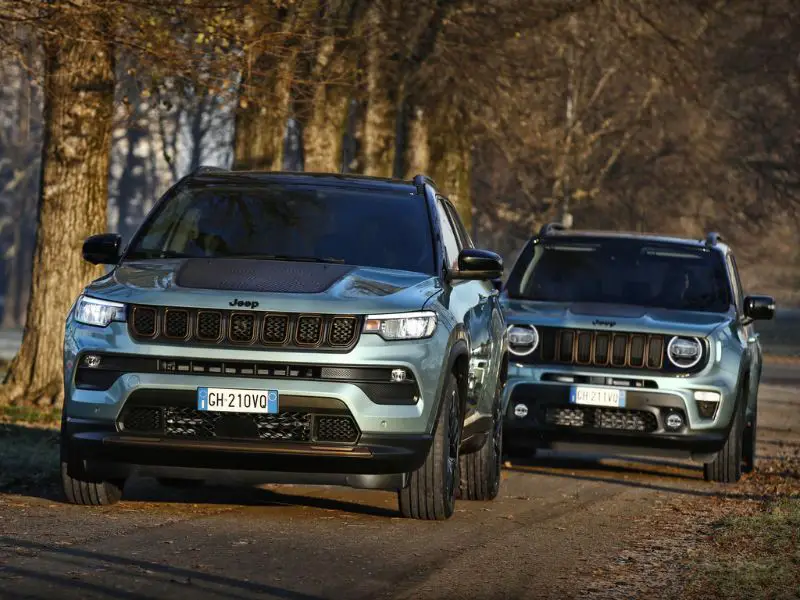 2022 metallic light blue jeep renegade and compass e hybrid driving next to a row of trees