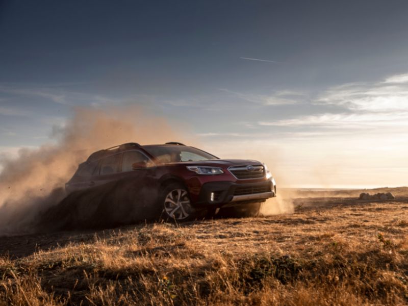 2022 red subaru outback limited kicking up some dust in a field