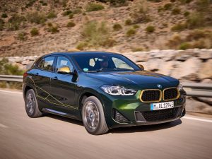 2022 metallic green and gold bmw x2 goldplay edition driving in a dessert environment on a b road